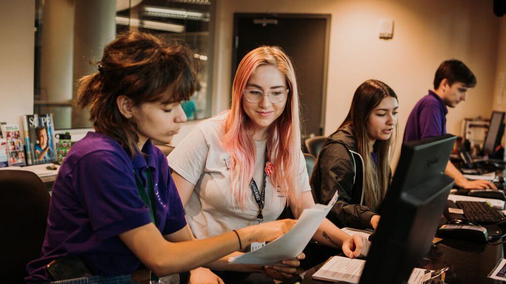 Customer service employee instructing an intern at the front desk.