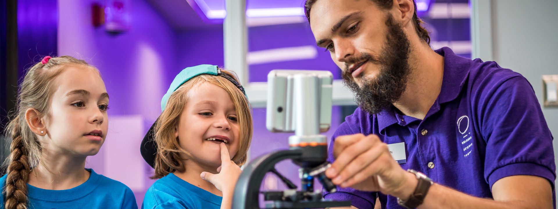 An educator shows two children in summer camp a cell in a microscope.