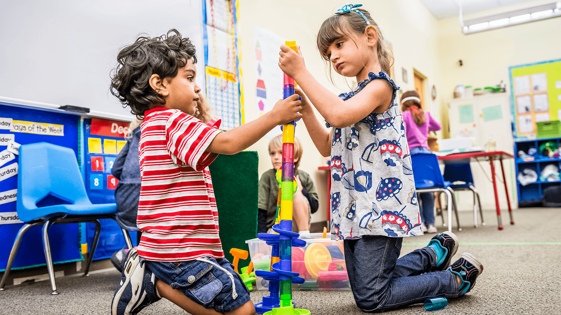 Two preschoolers build a tower together with small blocks.