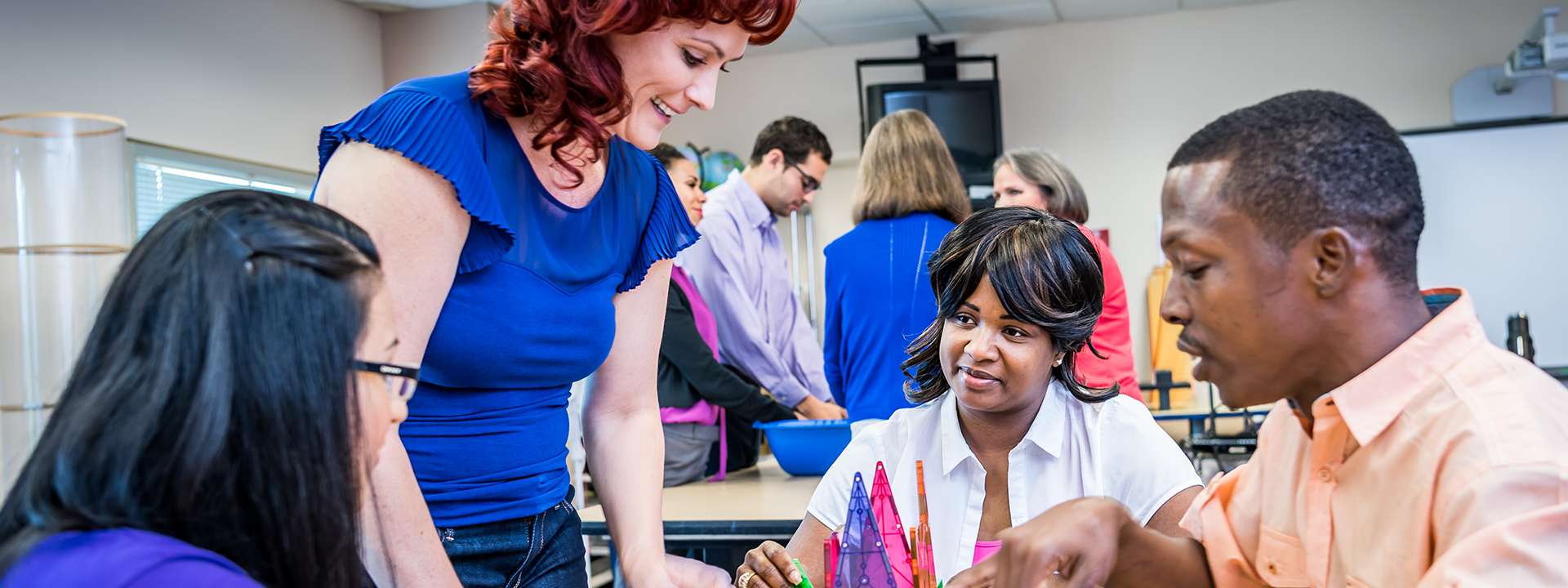 Adults in the educator professional development program exploring educational toys like magnetic blocks.