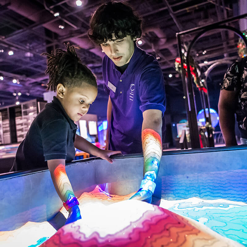 An employee shows a child the topographical sand exhibit.