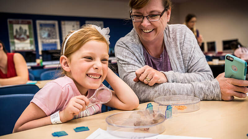 Mother and daughter during an activity. Daughter is holding a magnifying glass