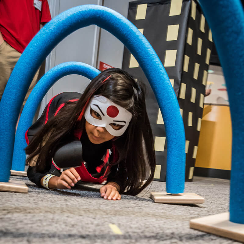 Child in superhero costume navigating obstacle course at Science Center