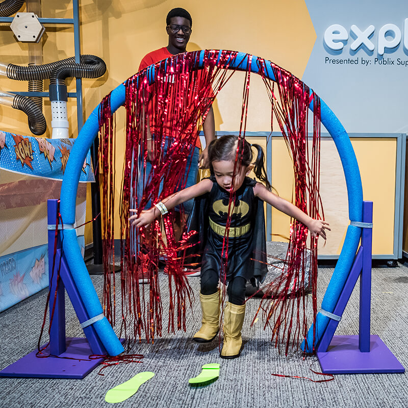 Child in Batgirl costume navigating obstacle course at Science Center
