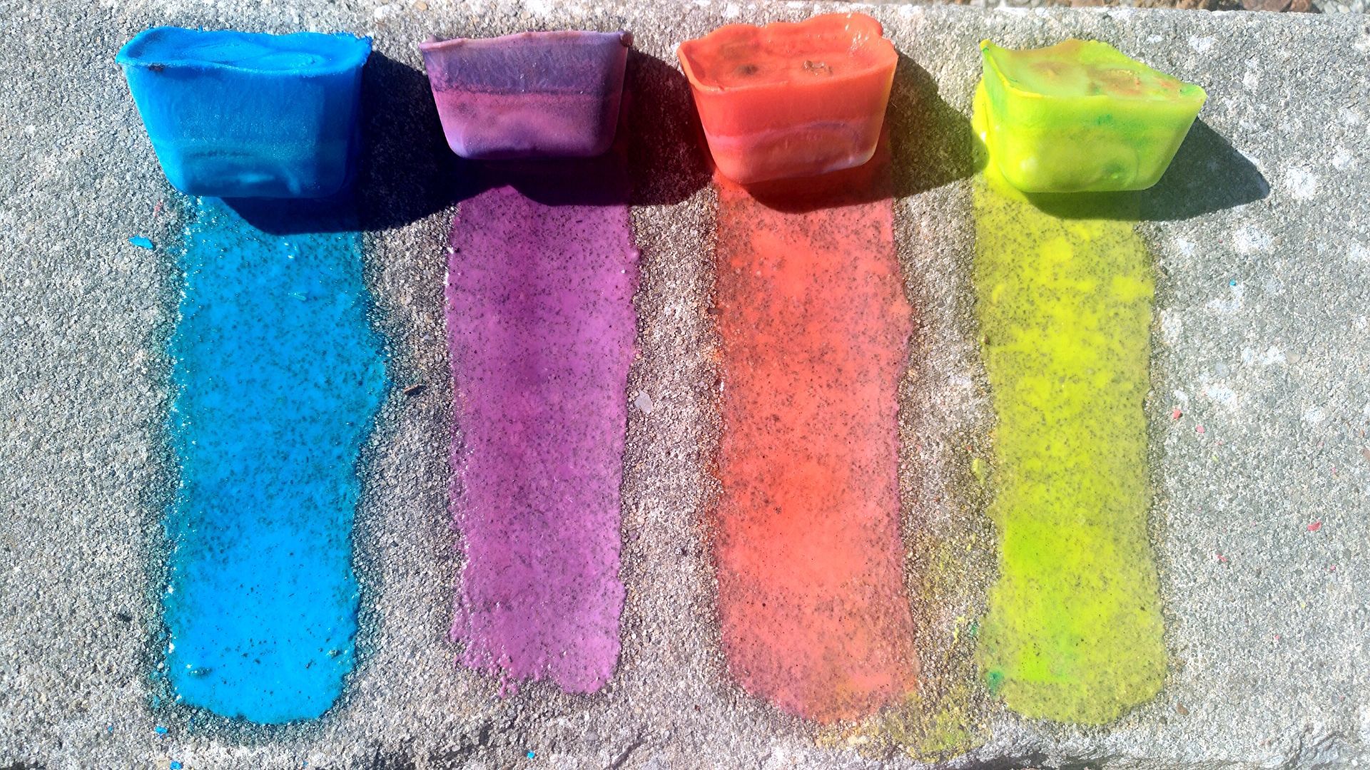 Four ice chalks drawn in rainbow pattern on sidewalk