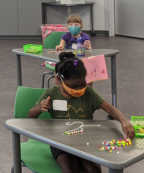Young children engaged in STEM activity at their desks in social distant camp classroom.