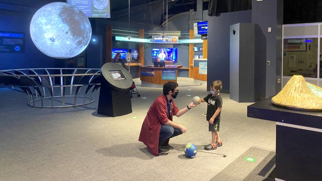 An OSC Science Program Interpreter shows a young child a model of Mars during a Space Tour.