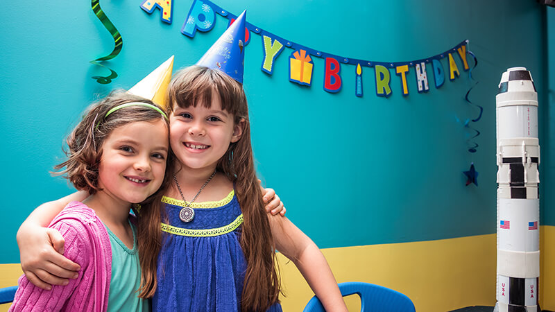 Two young children smiling and hugging during a birthday party at Orlando Science Center.