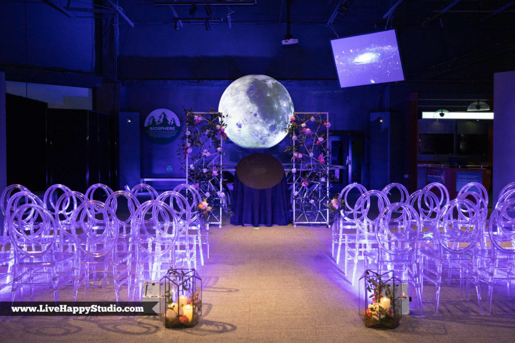 chairs set up for a wedding with purple lighting and a moon backdrop 