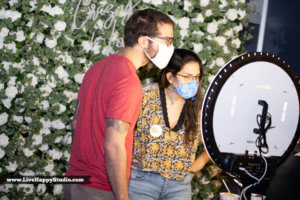 a couple taking a selfie in front of a white rose flower wall