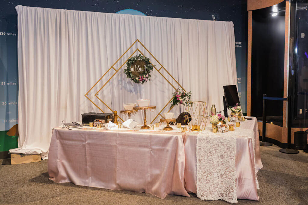 a table with pink cloth decorated with food and flowers