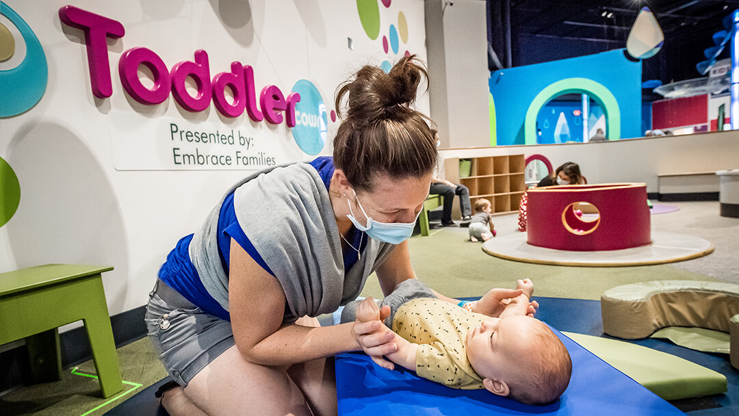 Caregiver playing with baby on foam play mat in Orlando Science Center Toddler playspace