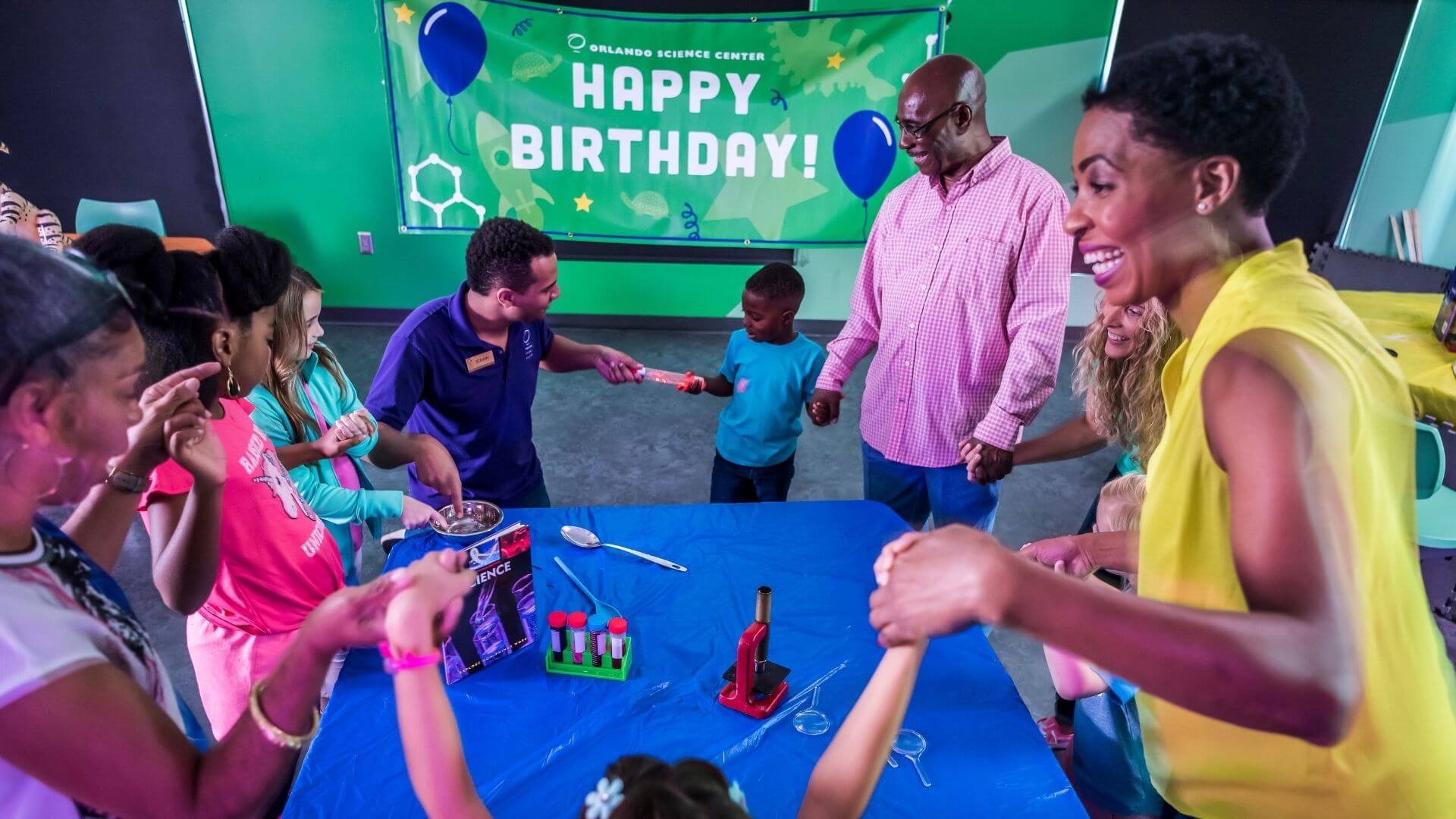 a group of kids and adults at a birthday party doing an experiment conducting electricity
