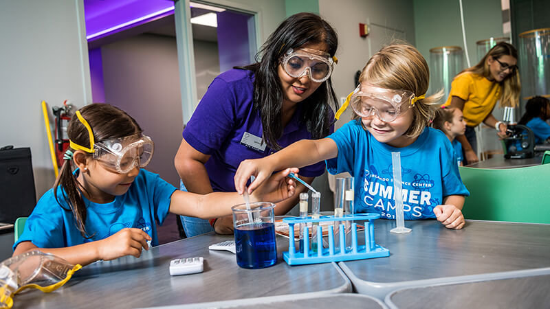 Instructor helping girl measure ingredients in a beaker at summer camp.
