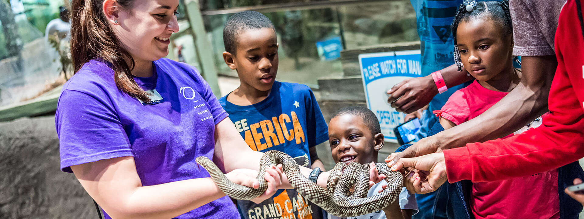 Family handling a snake with staff member during animal encounter in NatureWorks.