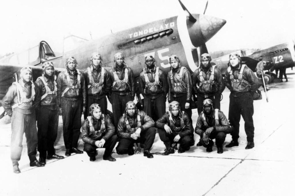 a photo of a dozen Red Tail pilots standing in front of a plane 
