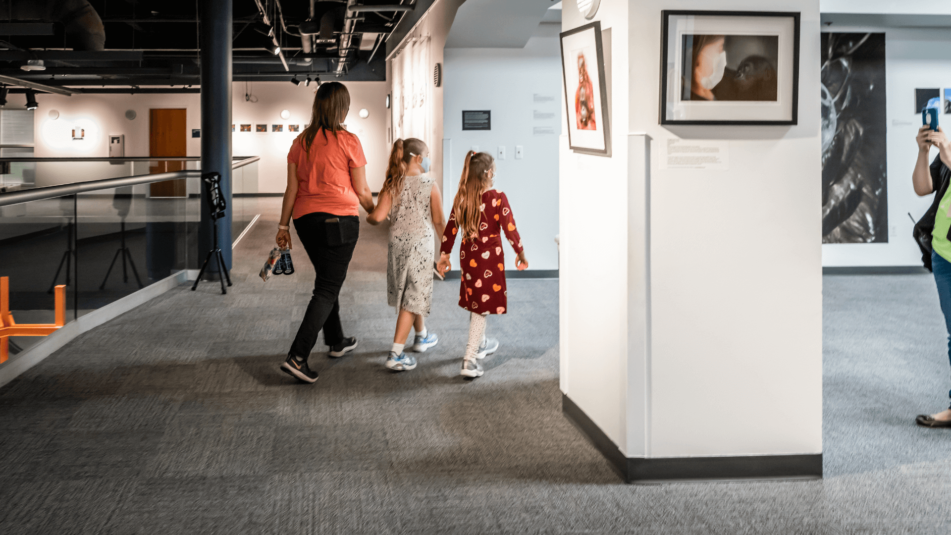 A woman and two young girls stroll through an art gallery