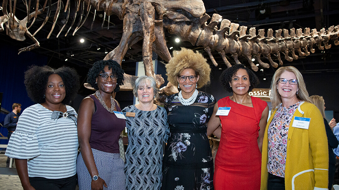 Inspire Science Breakfast guests gathered in front of T rex exhibit with Orlando Science Center CEO JoAnn Newman.