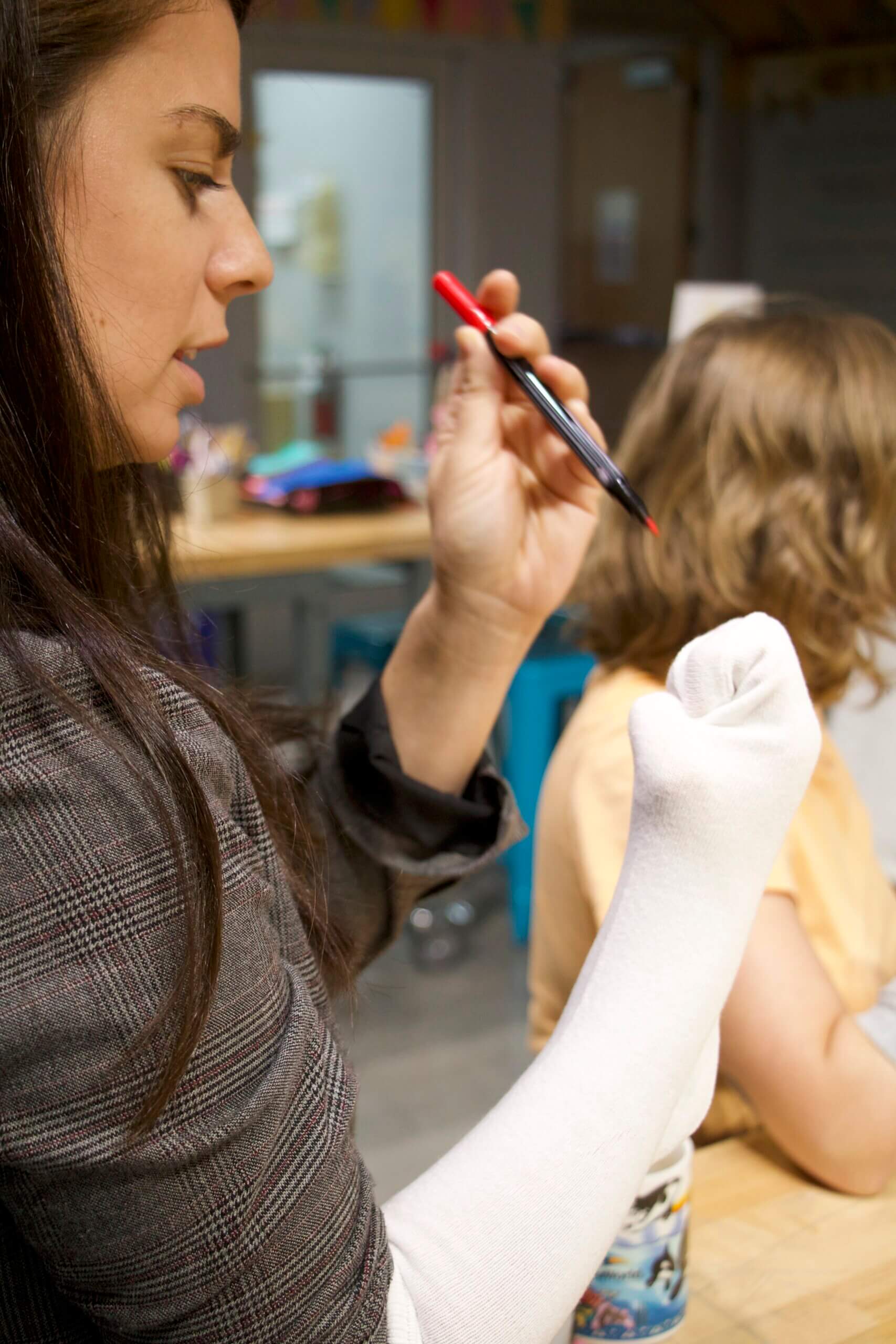 A woman draws eyes on a sock puppet using a fabric marker.