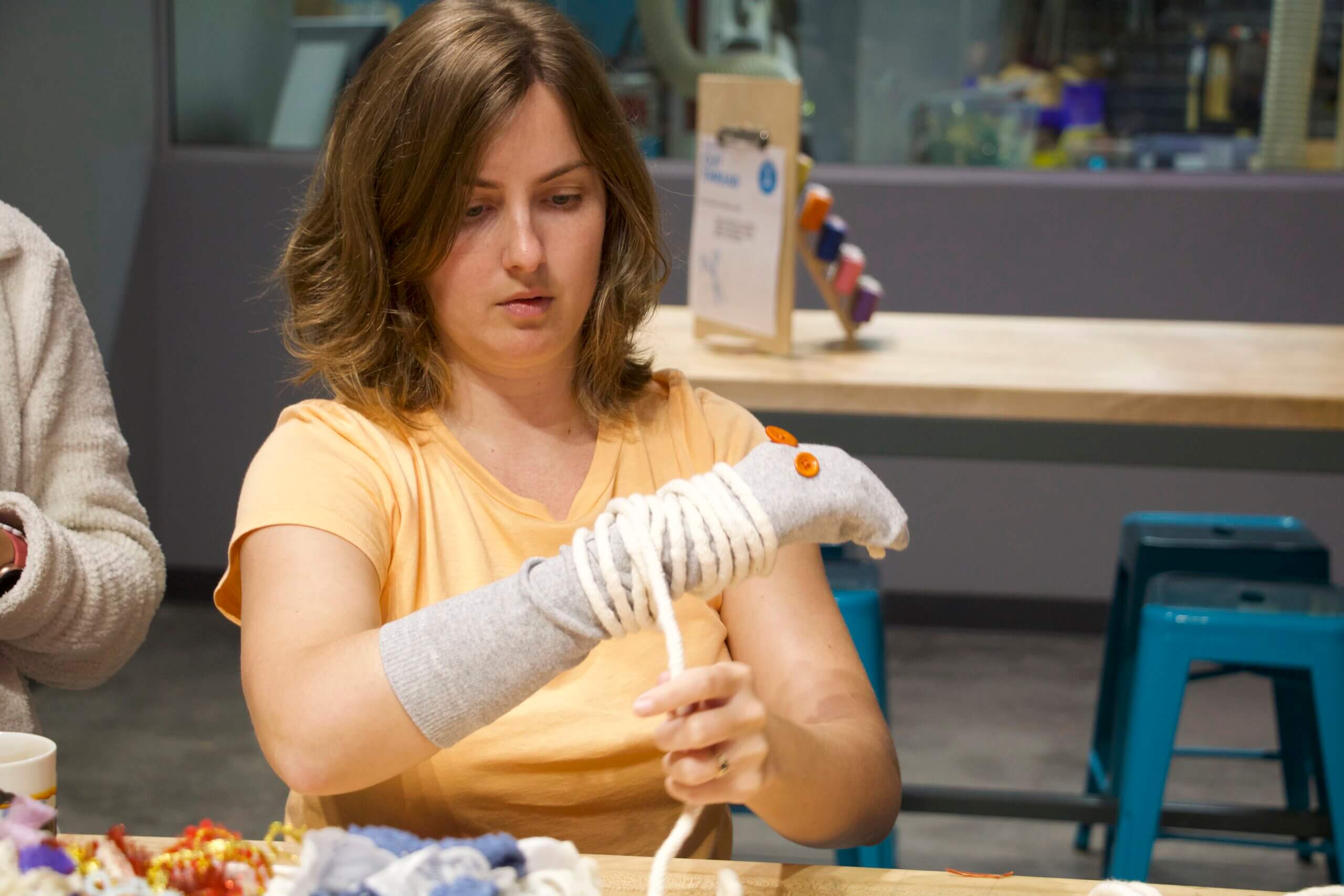 a woman wraps yarn around a sock puppet