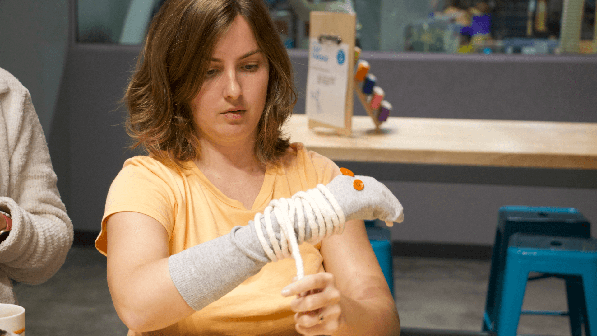 A woman wraps twine around a sock on her arm to create a mummy sock puppet.