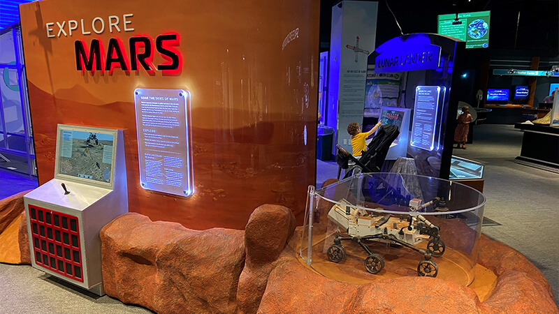 Explore Mars exhibit photo showing simulation game cabinet on large exhibit wall mural.