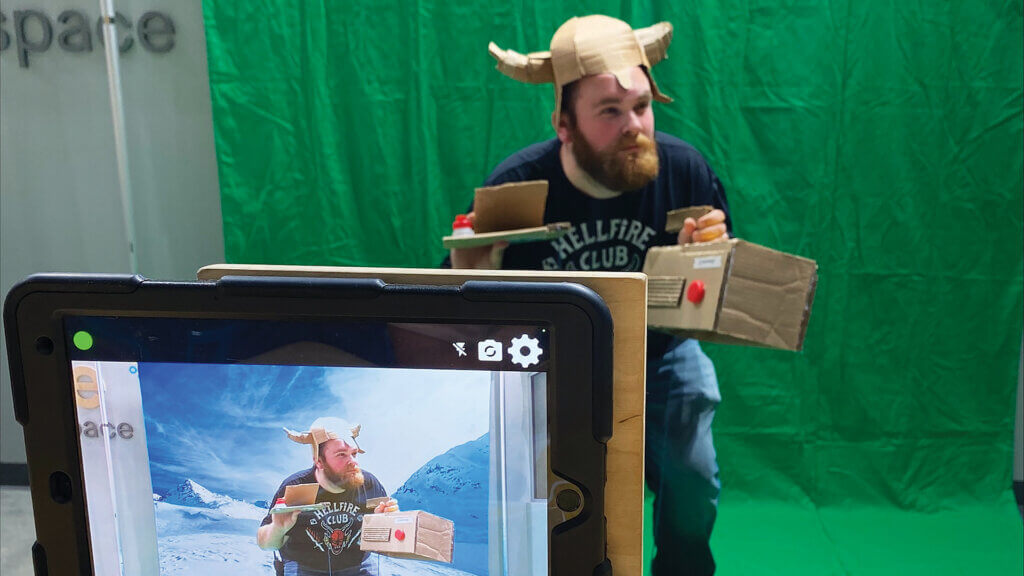 Person posing for a Minute Movie in The Hive: A Makerspace using a green-screen backdrop and cardboard props.