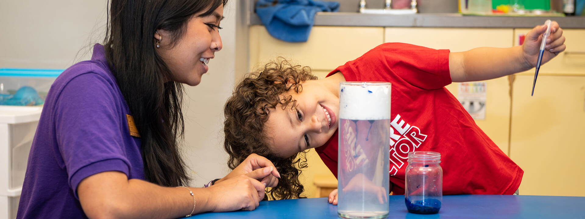 A preschool child and teacher excited about the success of a science experiment.