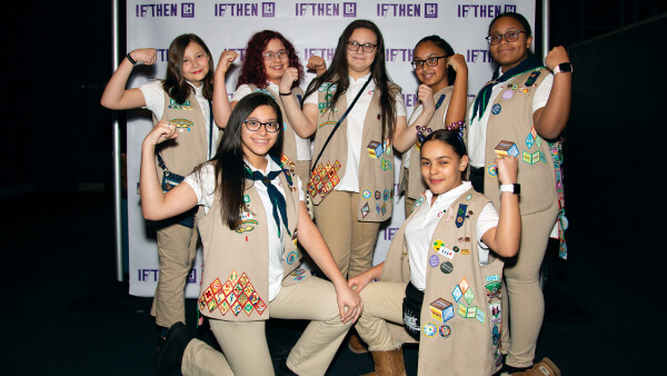 Girl Scout trope posing in front of photo wall at an If Then event.