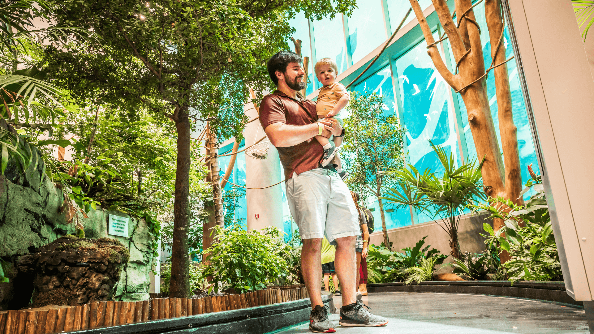 A father holds a young boy in a rainforest exhibit