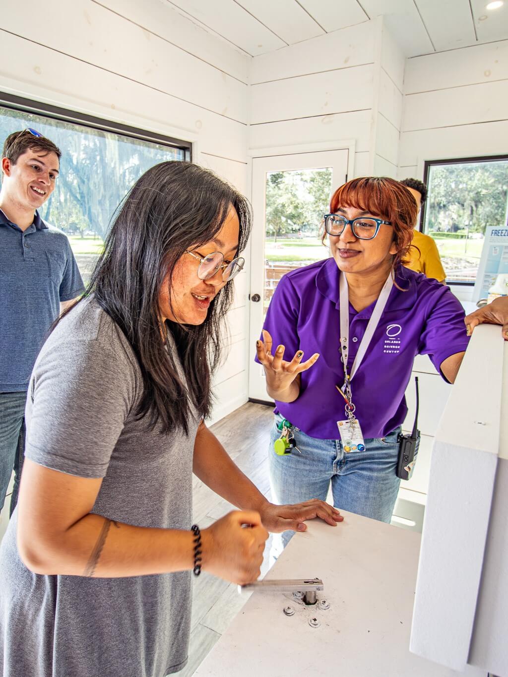 Two young women interact with an exhibit about energy used by light bulbs