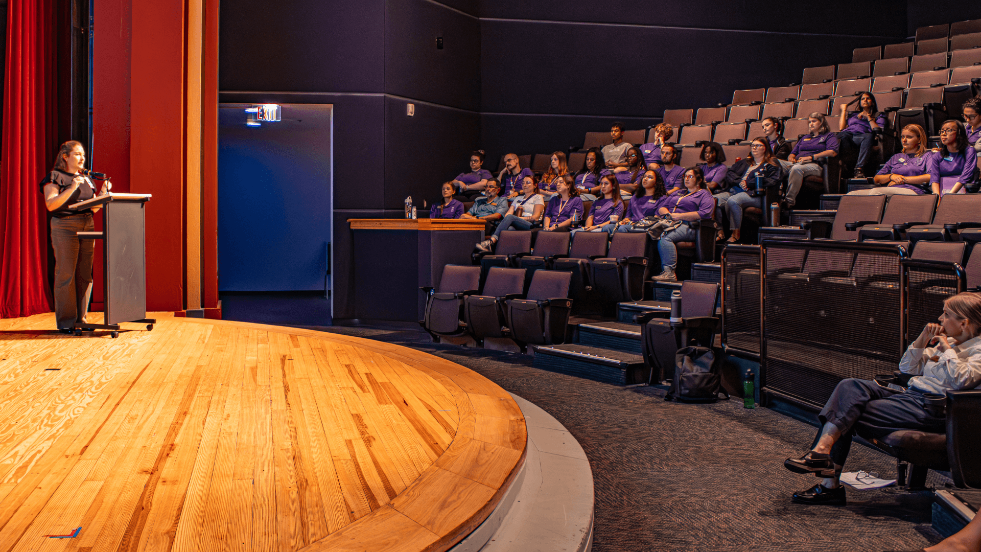A woman stands on a stage and lectures to a room of Science Center staff
