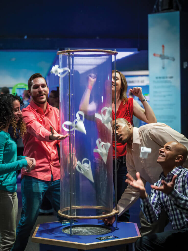 Adults interacting paper gliders in with wind tubes exhibit.