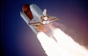 A space shuttle rises into the sky on a rocket spewing fire.