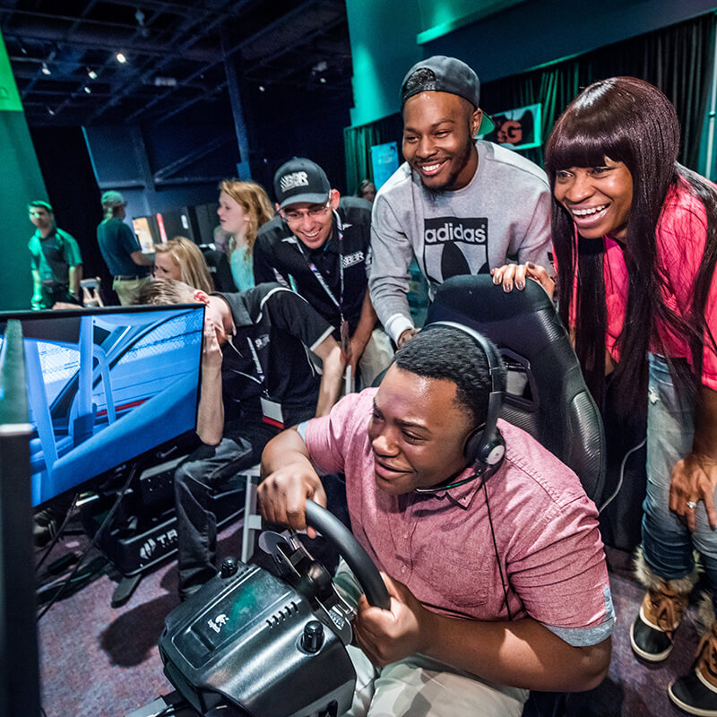 Guests encourage their friend as he drives a virtual race car.